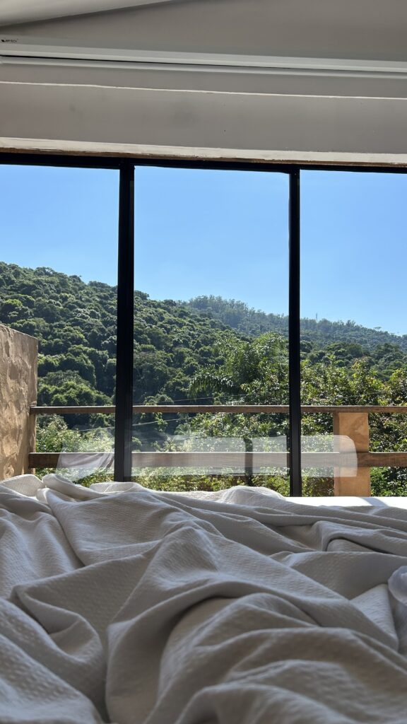 Hotel room view from bed looking out at jungle-covered hills through floor-to-ceiling windows