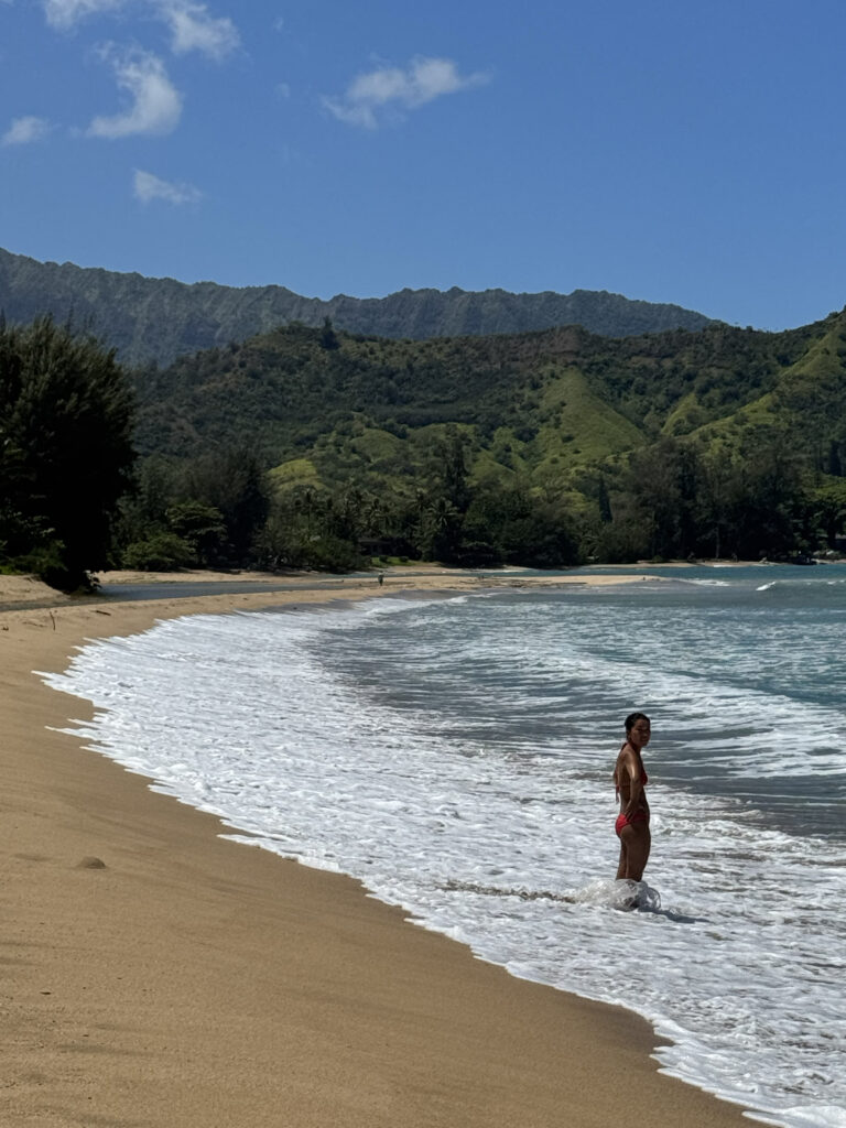 Woman walking along Hanalei Bay beach with green mountains in background
