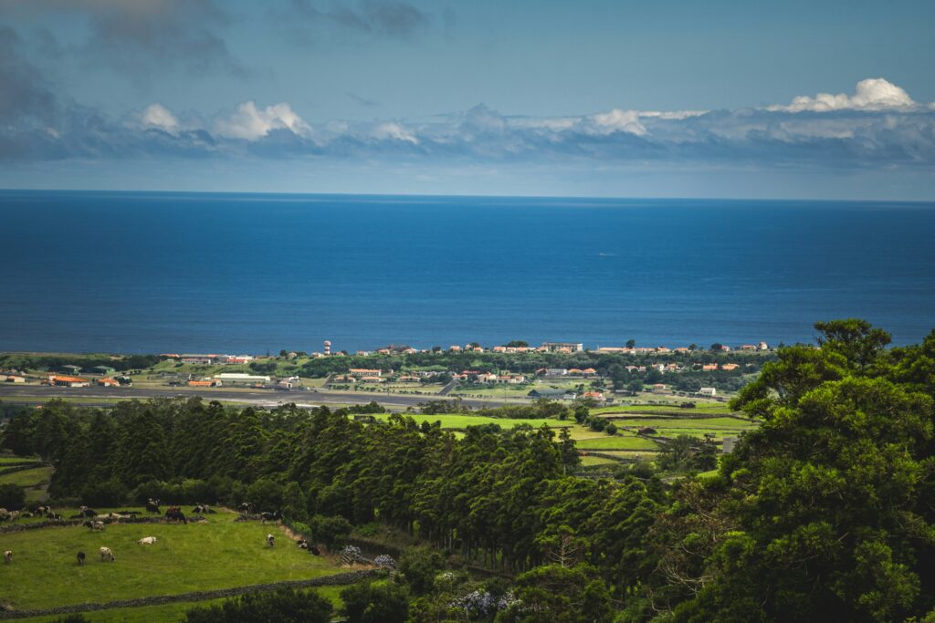 Lush green hillside with an Azores town in the distance on the edge of the vast Atlantic Ocean